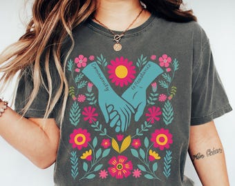Puede incluir: Una camiseta gris oscuro con un diseño floral y el texto "Community is Resilience".