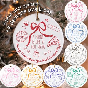 May include: White ceramic Christmas ornament with a red bow and the text "A FRIEND IS LIKE A HOT PIZZA." Additional designs include "eggnog," "candy cane," "good coffee," "fine wine," "chili pepper," "taco," and "pickle." The text "8 print color options" and "18 designs available" are also present.