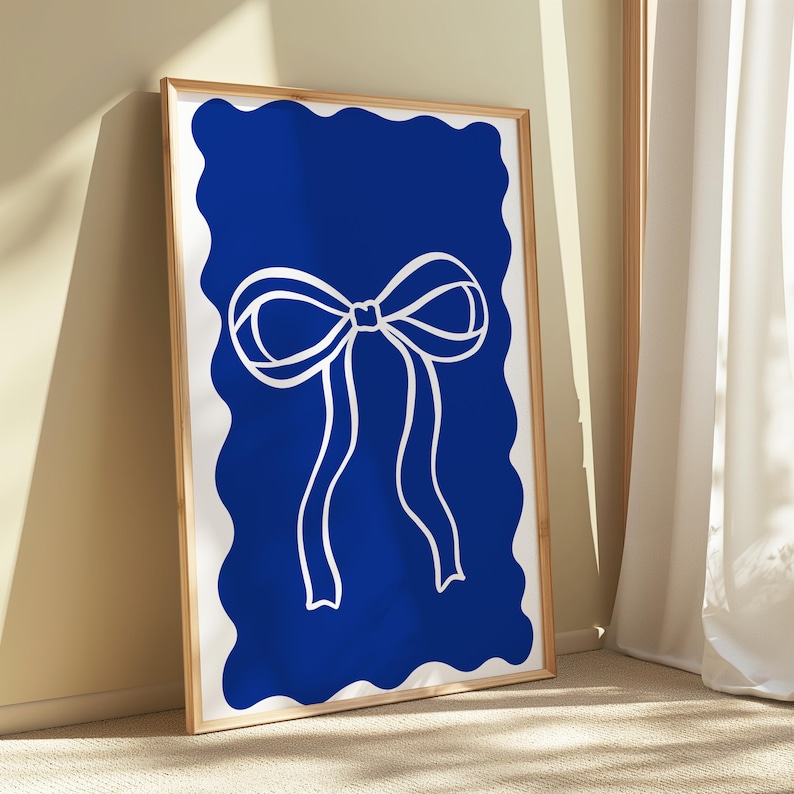 May include: A framed art print featuring a white bow design on a vibrant blue background. The bow is centered, with flowing ribbons. The blue background has a wavy, irregular border. The frame is a light wood color.