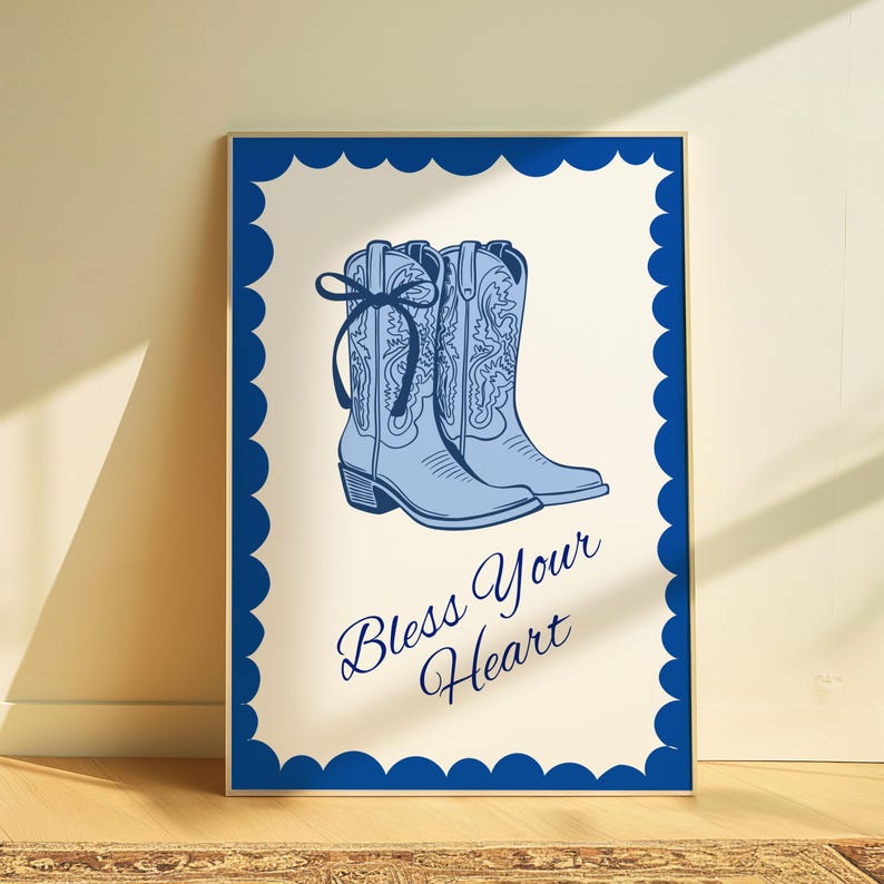 May include: A framed print featuring light blue cowboy boots with decorative stitching and a bow. The boots are set against a cream background with the phrase "Bless Your Heart" in a script font. The frame is a dark blue scalloped edge.