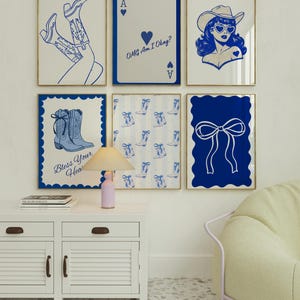 May include: Six framed art prints with blue and white designs. The prints include a pair of cowboy boots, a playing card with text, a cowgirl, a pair of boots with text, a pattern of boots, and a bow. The frames have gold trim.