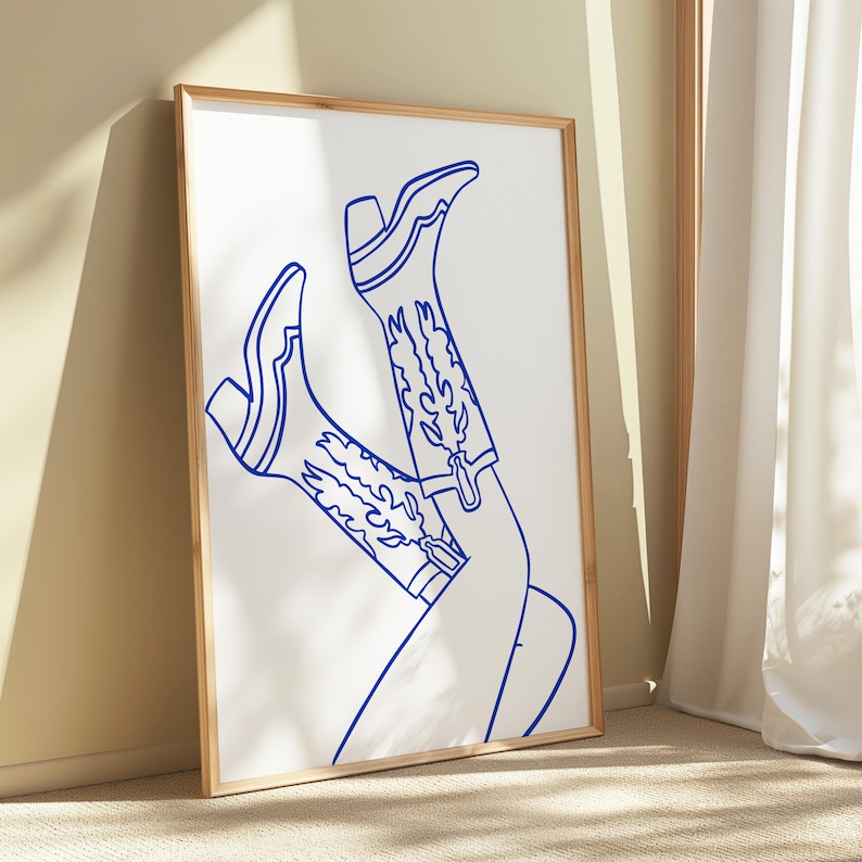 May include: A framed art print featuring a blue line drawing of a pair of cowboy boots. The boots are detailed with decorative stitching and a buckle, set against a white background. The artwork is in a wooden frame.