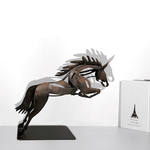 May include: A rusty brown metal sculpture of a horse leaping forward. The horse is on a black base. The sculpture is on a white surface.
