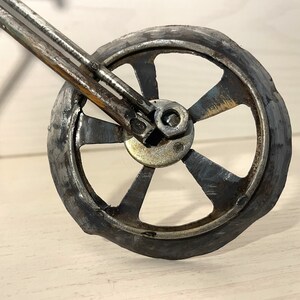 Op de afbeelding: Close-up van een metalen motorfietswiel met vijf spaken. Het wiel is gemaakt van gerecycled metaal en heeft een rustieke, industri&euml;le uitstraling.
