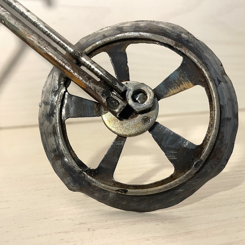 Op de afbeelding: Close-up van een metalen motorfietswiel met vijf spaken. Het wiel is gemaakt van gerecycled metaal en heeft een rustieke, industri&euml;le uitstraling.