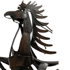 May include: A black metal sculpture of a horse's head with a stylized mane. The sculpture is made of recycled metal and has a rustic, industrial look.