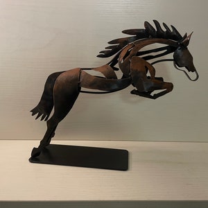 May include: A metal sculpture of a horse leaping into the air. The horse is made of brown and black metal and is mounted on a black base.