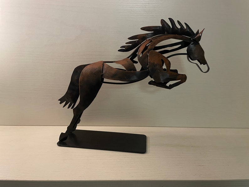 May include: A metal sculpture of a horse leaping into the air. The horse is made of brown and black metal and is mounted on a black base.