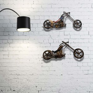 Op de afbeelding: Twee metalen motorfiets wandsculpturen in een rustieke bruine afwerking. De motorfietsen zijn in chopper-stijl met een lange voorvork en een enkel zadel. De bovenste motorfiets heeft een Amerikaans vlagontwerp op de tank.