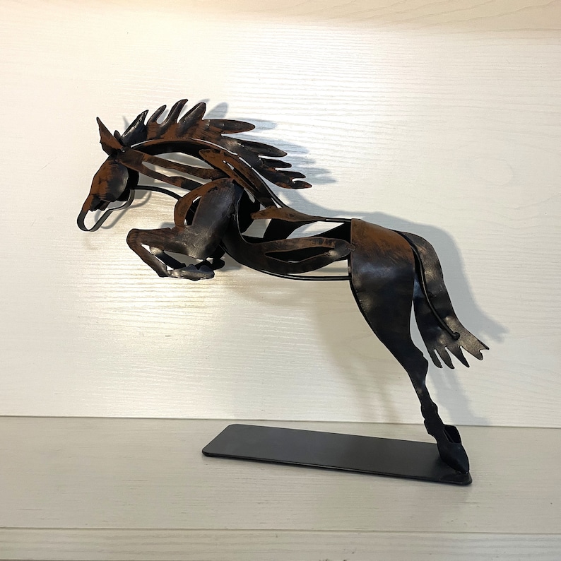 May include: A metal sculpture of a brown horse leaping into the air. The horse is made of thin metal and has a detailed, intricate design. The sculpture is mounted on a black base.