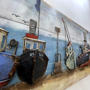 Peut inclure: Une &oelig;uvre d'art murale en bois repr&eacute;sentant cinq bateaux en m&eacute;tal align&eacute;s. Les bateaux sont peints dans diff&eacute;rentes couleurs, notamment le bleu, le vert, le rouge et le noir. Les bateaux portent des noms, dont "SIO SIO", "NET" et "FISH".