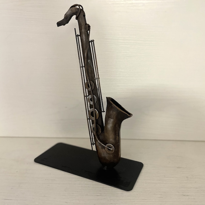 May include: A metal sculpture of a saxophone in a dark brown finish. The saxophone is standing on a black metal base.