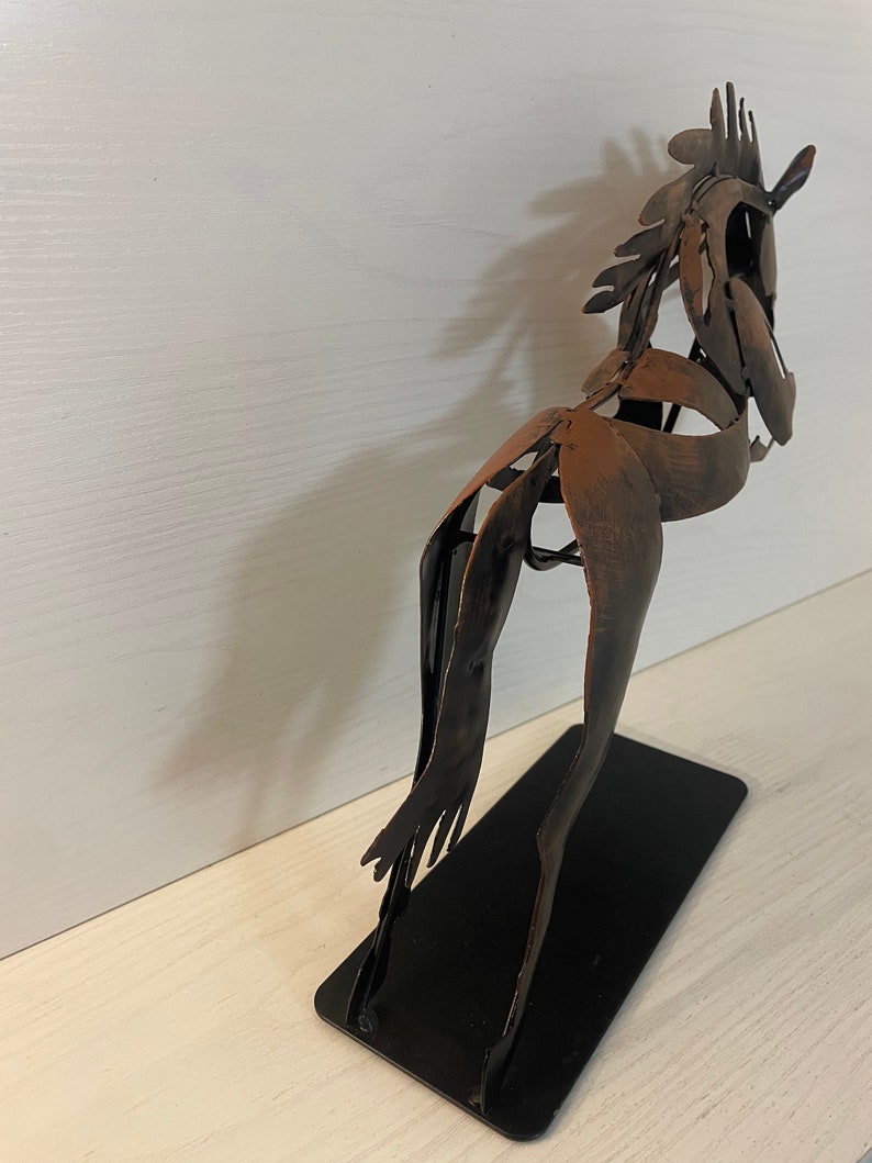 May include: A metal sculpture of a horse in a brown and black finish. The horse is standing on a black metal base.