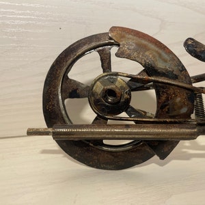 May include: A rusty metal motorcycle sculpture with a single wheel, a seat, and a handlebar. The sculpture is made of recycled metal and has a rustic, industrial look.