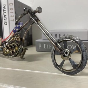 Op de afbeelding: Een metalen sculptuur van een motorfiets met een Amerikaans vlagontwerp op de stoel. De motorfiets is gemaakt van gerecycled metaal en heeft een rustieke uitstraling.
