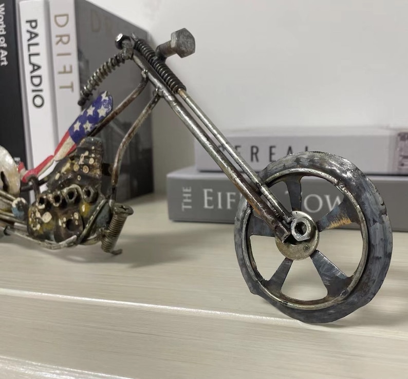 Op de afbeelding: Een metalen sculptuur van een motorfiets met een Amerikaans vlagontwerp op de stoel. De motorfiets is gemaakt van gerecycled metaal en heeft een rustieke uitstraling.