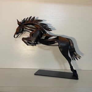 May include: A black metal sculpture of a horse leaping into the air. The horse is made of thin, twisted metal and has a rustic finish.