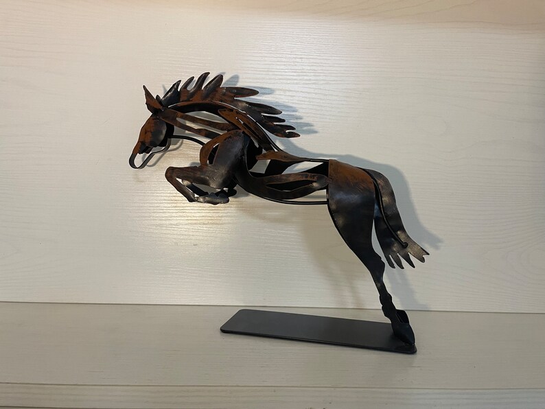 May include: A black metal sculpture of a horse leaping into the air. The horse is made of thin, twisted metal and has a rustic finish.