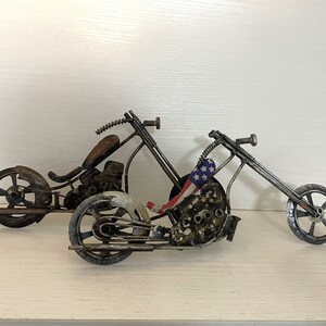 Op de afbeelding: Twee handgemaakte motorfiets-sculpturen van metaal, een met een Amerikaans vlagontwerp. De motorfietsen zijn gemaakt van gerecyclede metalen onderdelen en hebben een rustieke, industri&euml;le uitstraling.