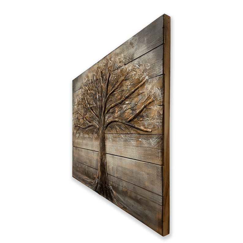 Op de afbeelding: Een bruine houten wanddecoratie met een 3D-reli&euml;f van een boom. De boom is geschilderd in tinten bruin en goud, en de achtergrond is lichtbruin met witte strepen.