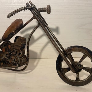 May include: A metal motorcycle sculpture made from recycled materials. The motorcycle is black and has a brown leather seat. The motorcycle has a single front wheel and a single rear wheel.