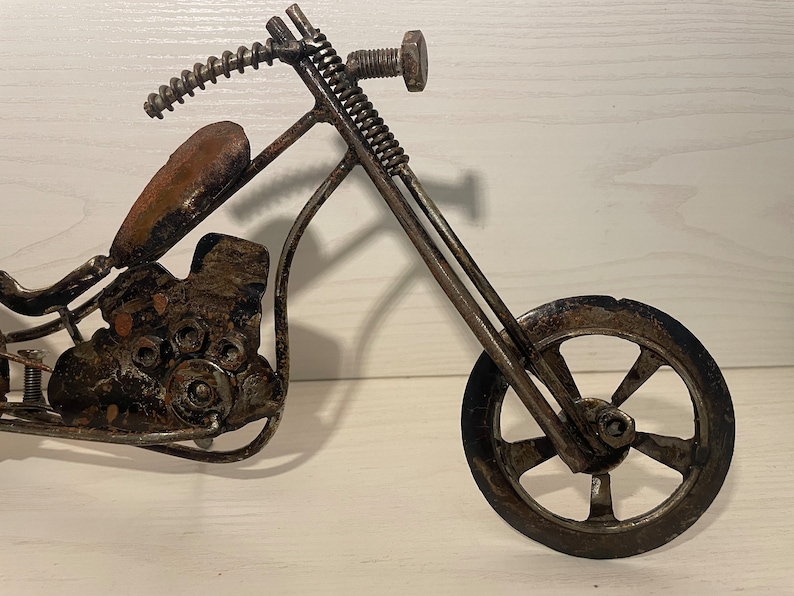 May include: A metal motorcycle sculpture made from recycled materials. The motorcycle is black and has a brown leather seat. The motorcycle has a single front wheel and a single rear wheel.