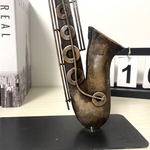 May include: A metal saxophone sculpture with a brown and gold finish. The sculpture is on a black base.