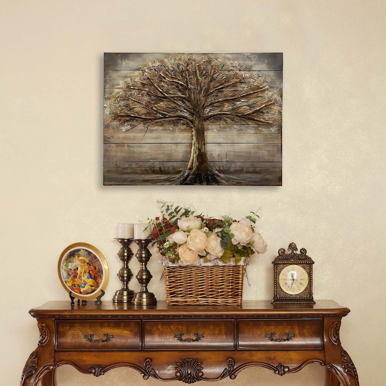 Op de afbeelding: Een houten wandkunstwerk met een bruine boom met gouden accenten. De boom is geplaatst tegen een rustieke houten achtergrond. Het kunstwerk wordt tentoongesteld op een houten consoletafel met een vaas met witte bloemen, een decoratief bord en een klok.