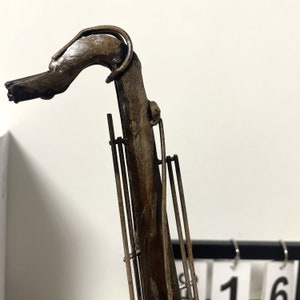 May include: A metal sculpture of a saxophone with a brown and black finish. The sculpture is made of thin metal rods and has a detailed design.