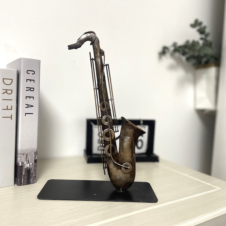 May include: A metal saxophone sculpture with a brown and gold finish. The sculpture is standing on a black base.