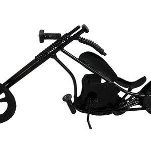May include: A black metal motorcycle sculpture with a detailed design. The motorcycle has a long, curved frame and two wheels with a spoke design. The sculpture is made of recycled metal and is a unique and interesting piece of art.