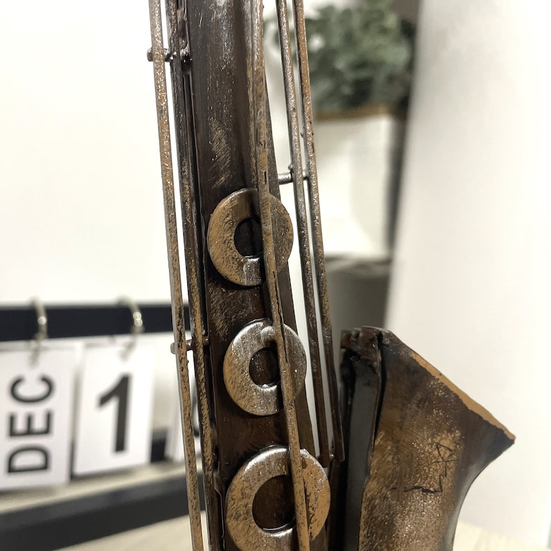 May include: A metal saxophone sculpture with a brown and gold finish. The sculpture has a detailed design with multiple rings and a bell.