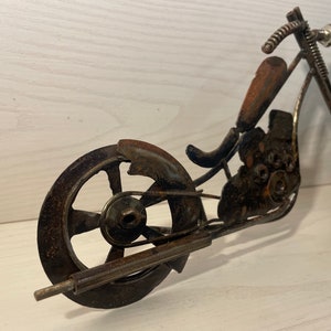May include: A rusty metal motorcycle sculpture with a spring-like handlebar and two wheels. The motorcycle is made of various metal pieces, including nuts, bolts, and washers.
