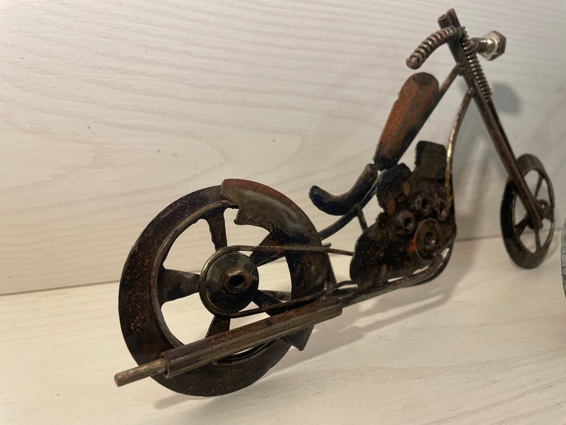May include: A rusty metal motorcycle sculpture with a spring-like handlebar and two wheels. The motorcycle is made of various metal pieces, including nuts, bolts, and washers.