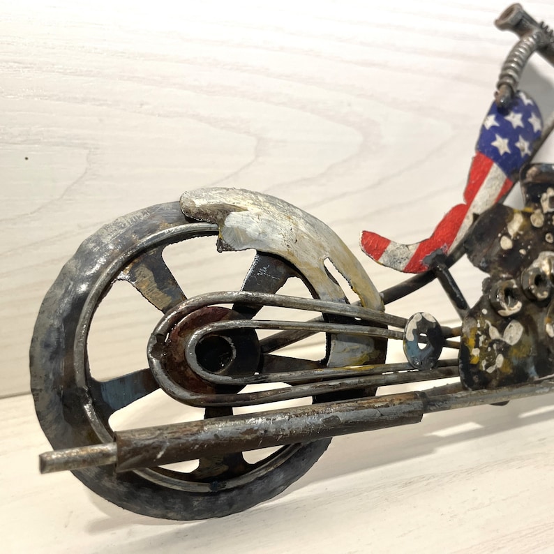 Op de afbeelding: Een metalen sculptuur van een motorfiets met een Amerikaans vlagontwerp. De motorfiets is gemaakt van gerecycled metaal en heeft een robuuste, industri&euml;le uitstraling.