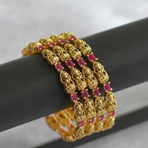 Peut inclure: Ensemble de quatre bracelets en or avec des motifs complexes et des pierres précieuses roses. Les bracelets sont empilés les uns sur les autres.