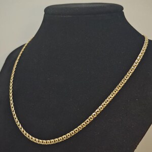 May include: A gold-coloured chain necklace with a detailed, textured design. The necklace is displayed on a black mannequin, showcasing its intricate links and overall aesthetic. The chain is a classic jewellery piece.