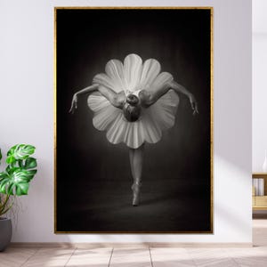 Peut inclure: Une photographie en noir et blanc d'une ballerine portant un tutu blanc, effectuant une pose la tête baissée et les bras tendus. La ballerine est debout sur une jambe, l'autre jambe étant tendue derrière elle.
