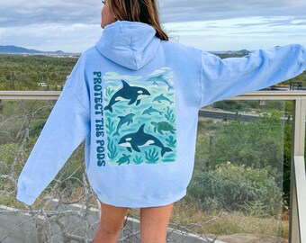 May include: Light blue hoodie with a graphic of orcas, turtles, and other marine life. The text "PROTECT THE PODS" is printed vertically on the left sleeve. The hoodie is a solid light blue color.