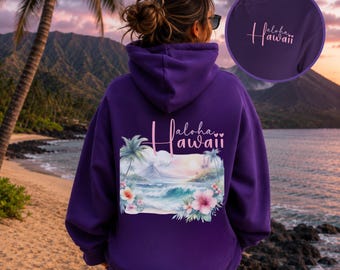 May include: A deep purple hooded sweatshirt featuring a back graphic of a tropical beach scene with palm trees, ocean waves, and hibiscus flowers. The text "aloha hawaii" is printed above the scene, with a smaller matching logo on the front chest.