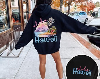 Puede incluir: Sudadera con capucha negra con un estampado gráfico de una escena de puesta de sol con palmeras y el texto "Aloha Hawaii" en la espalda. La sudadera se muestra siendo usada por una persona.