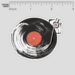 Op de afbeelding: Een sticker met een zwarte vinylplaat met een rode kern en een witte en grijze platenspeler. De plaat heeft een getextureerde, penseelstreekachtige uitstraling. De arm van de platenspeler is wit en het ontwerp heeft een vintage esthetiek.