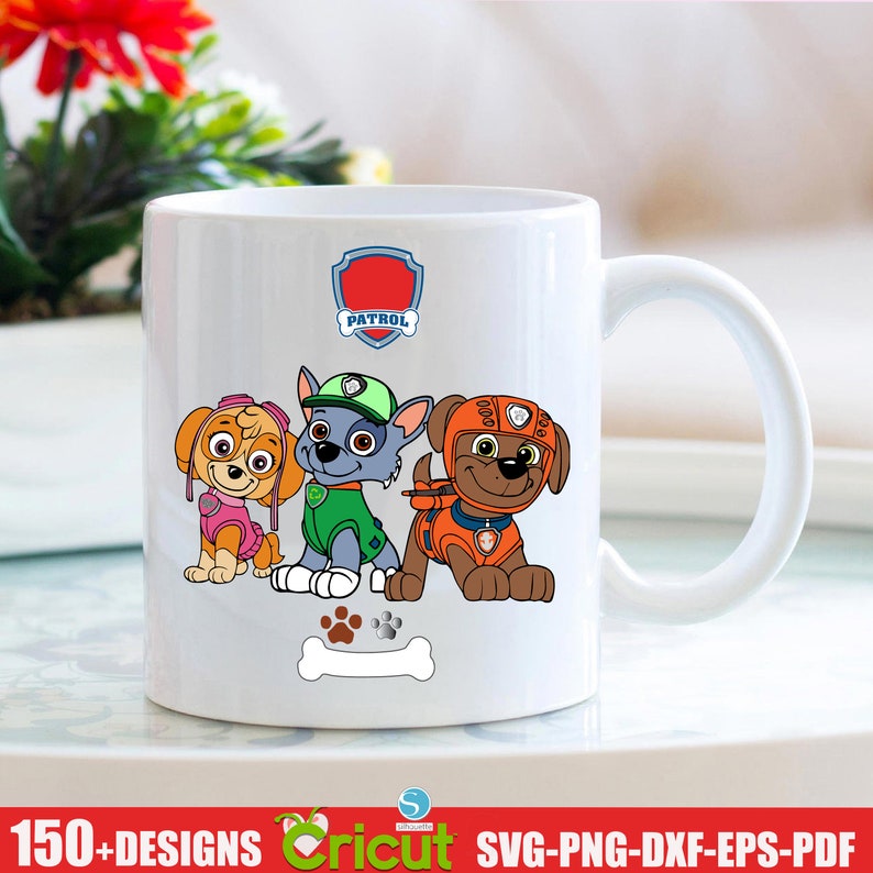 May include: White ceramic mug featuring a colourful image of three cartoon dogs from the Paw Patrol cartoon. The dogs are standing in a row with a bone in front of them. The text "PATROL" is in a red shield above the dogs.