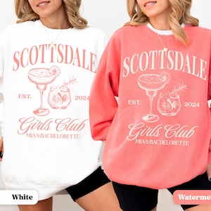 Puede incluir: Dos sudaderas blancas de cuello redondo con un dise&ntilde;o gr&aacute;fico rosa. El gr&aacute;fico presenta un vaso de c&oacute;ctel con una rodaja de lima y un vaso con cubitos de hielo. El texto en la sudadera dice "Scottsdale Est. 2024 Girls Club Mia's Bachelorette". Una sudadera es blanca y la otra es sand&iacute;a.