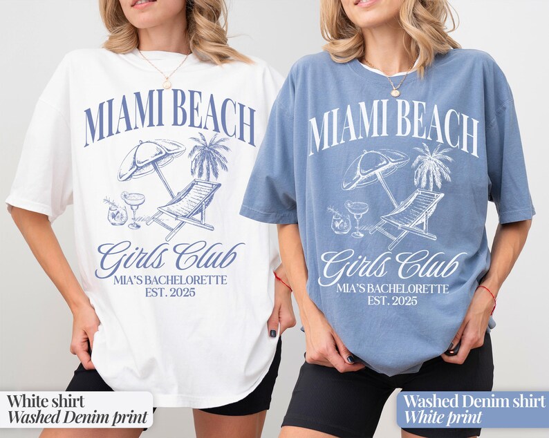 May include: Two t-shirts with a graphic print of a beach scene with a lounge chair, palm trees, and the text "Miami Beach Girls Club Mia's Bachelorette Est. 2025". One shirt is white with a blue print and the other is a washed denim blue with a white print.
