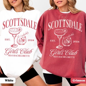 Puede incluir: Dos sudaderas blancas de cuello redondo con texto y gr&aacute;ficos rojos. El texto dice "Scottsdale Est. 2024 Girls Club Mia's Bachelorette". El gr&aacute;fico es de dos c&oacute;cteles. Una sudadera es blanca y la otra es carmes&iacute;.