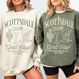 May include: Two women wearing cream and green sweatshirts with the text "Scottsdale Girls Club Mia's Bachelorette Est. 2024" and a graphic of a cactus, margarita, and cowboy boots.