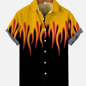 Puede incluir: Una camisa de manga corta con botones y un estampado de llamas negras y amarillas. La camisa tiene cuello y cierre de botones.
