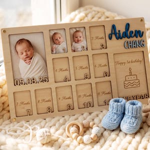 May include: A rectangular wooden baby milestone photo board featuring the name Aiden Chang in blue and grey, with slots for monthly photos, engraved numbers, a birthday cake graphic, and the text Happy 1st birthday and ONE YEAR.