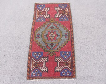 May include: A rectangular woven rug featuring a vibrant red background with a central geometric medallion in shades of gray, blue, and yellow. The rug includes four corner motifs with blue accents and a decorative border with fringe at both ends.